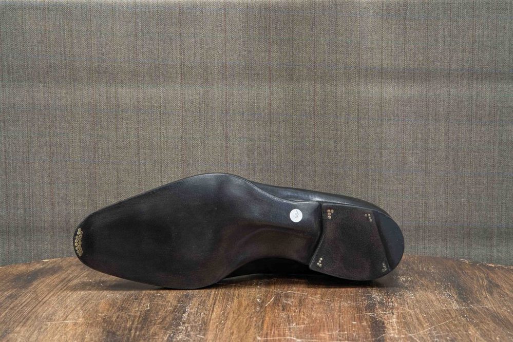 The image shows the black sole of a shoe with a circular label and metal studs.