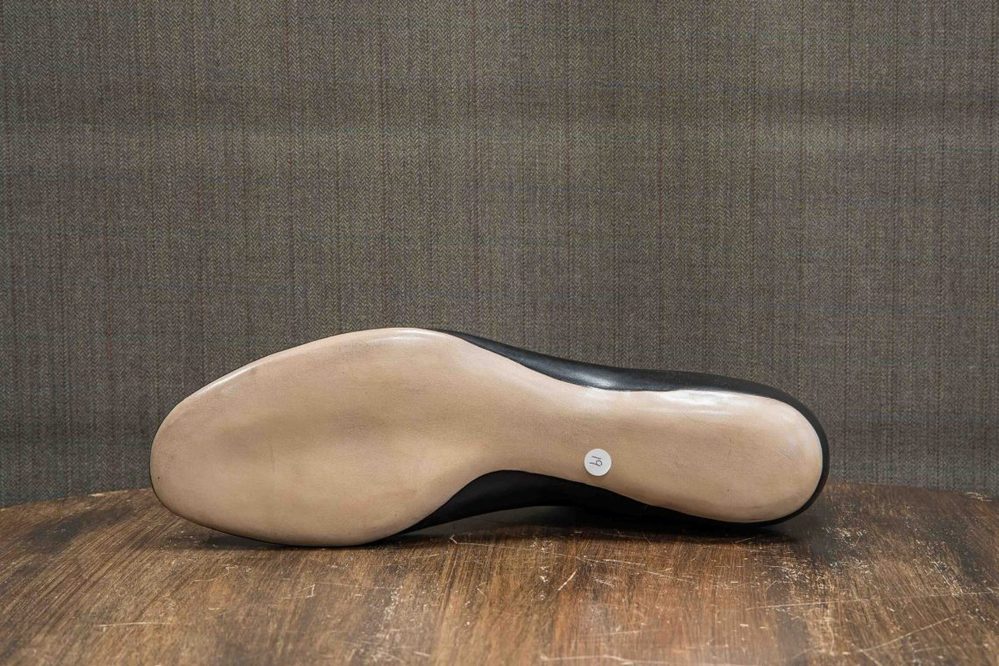 The image shows the sole of a black shoe with a smooth beige bottom and a circular label marked "14."