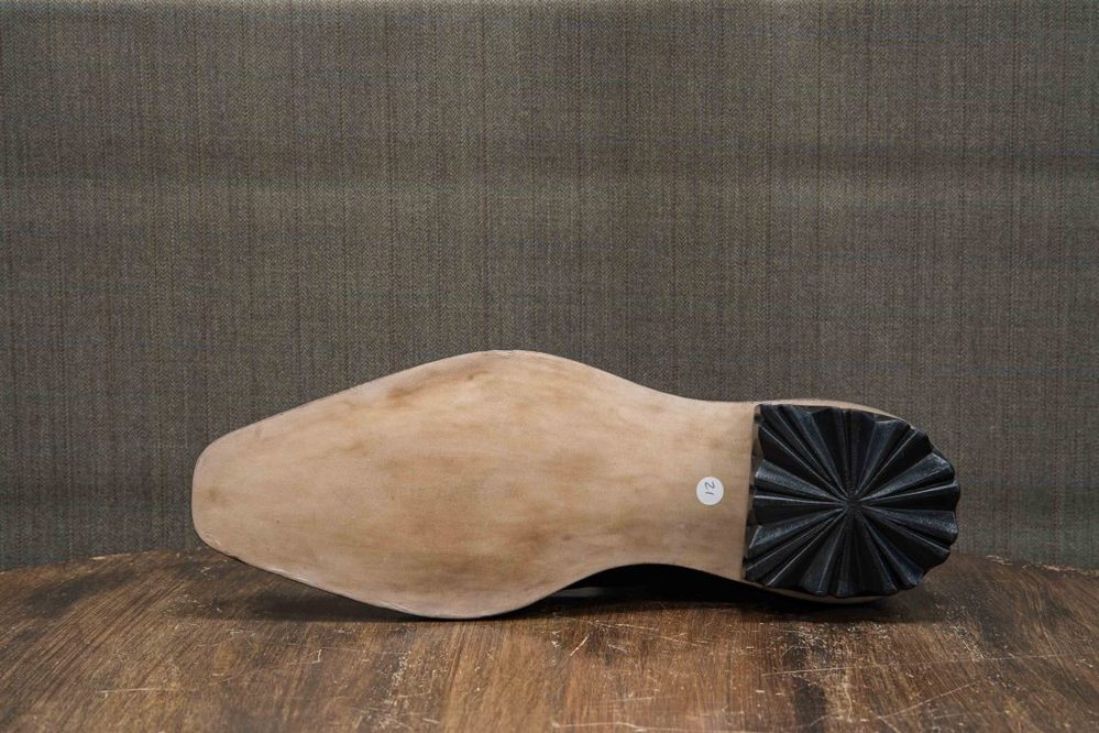 The image shows the sole of a shoe with a smooth beige surface and a black, ridged heel.