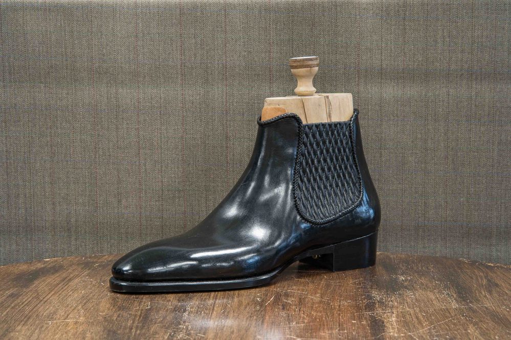 A black leather ankle boot with a textured side panel and a wooden shoe tree inserted inside.
