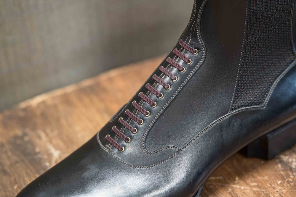 A close-up of a black leather shoe featuring burgundy laces and textured side panels.