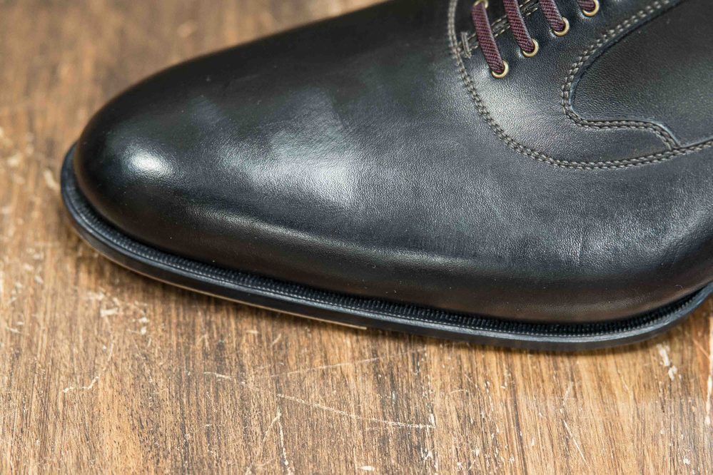 Close-up of a polished black leather shoe with burgundy laces.