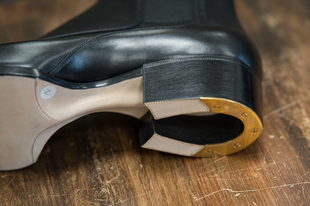 A close-up of a black leather shoe with a distinctive gold-accented heel.