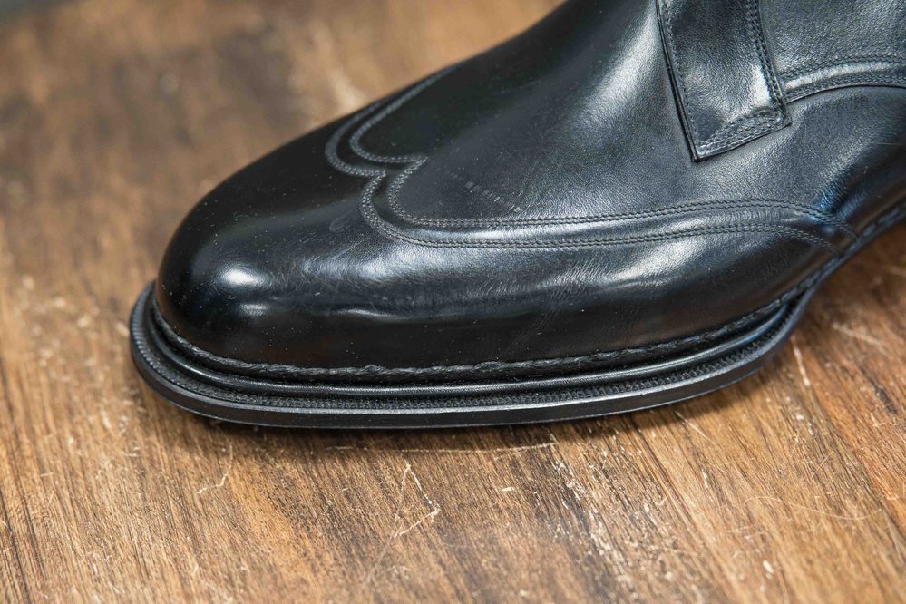 Close-up of a polished black leather shoe with decorative stitching along the toe.