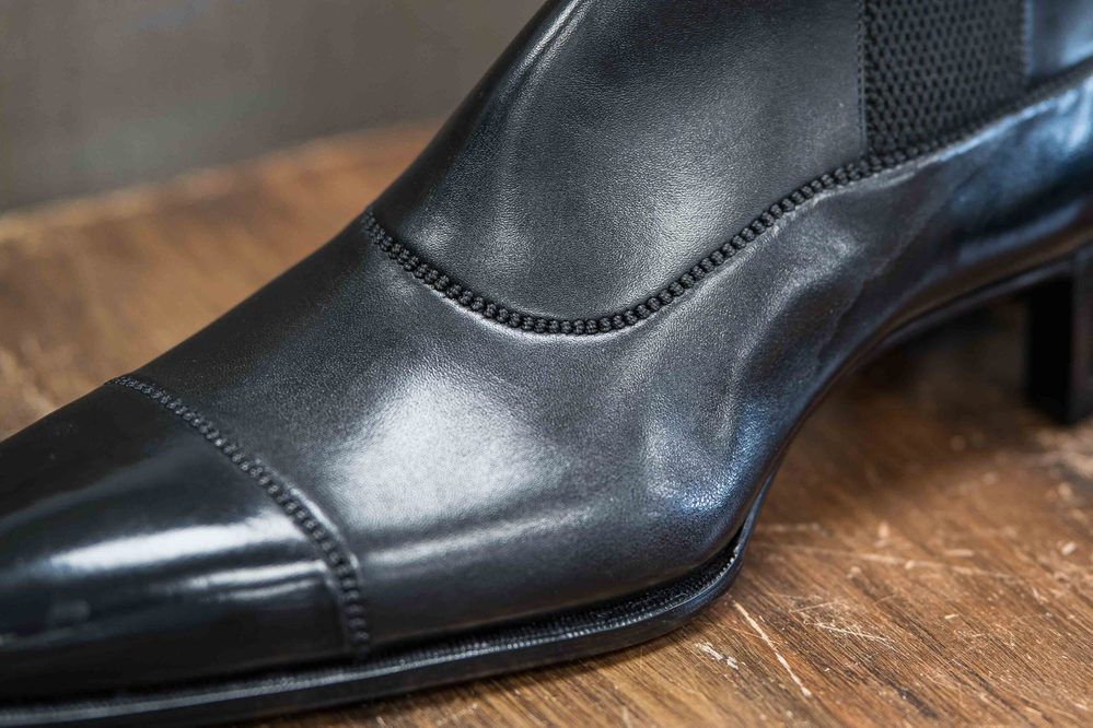 A close-up of a polished black leather shoe with detailed stitching and a pointed toe.