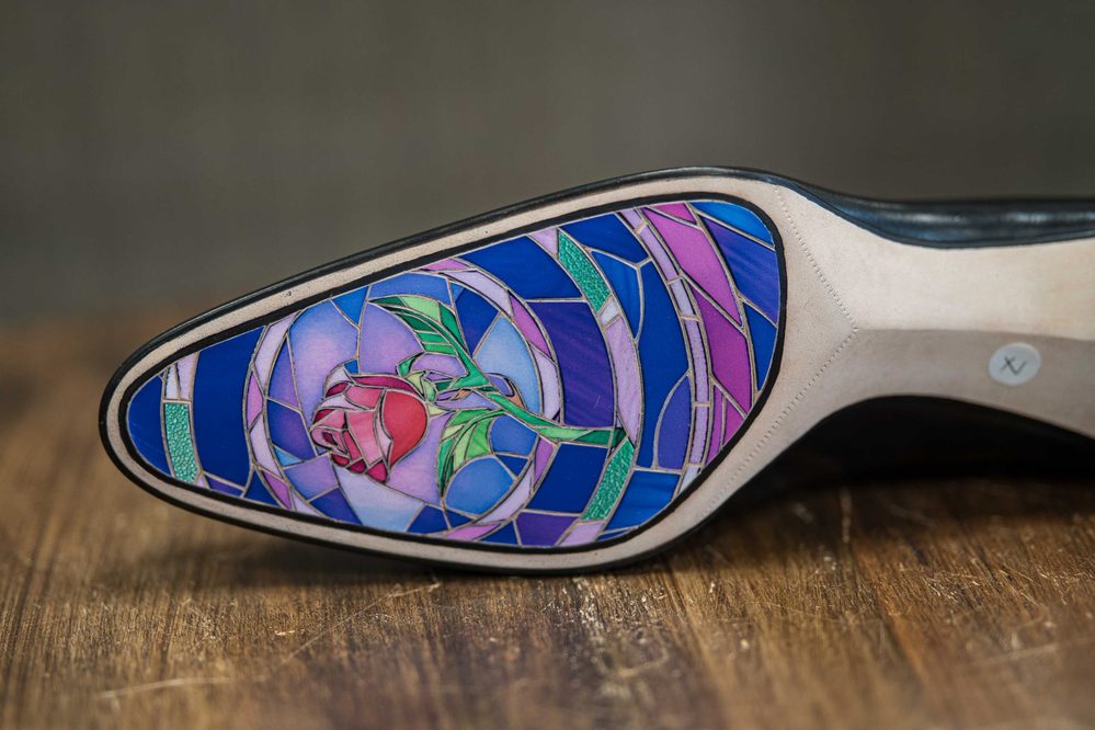 A close-up of a shoe sole featuring a colorful stained glass design with a red rose and blue, purple, and green accents.