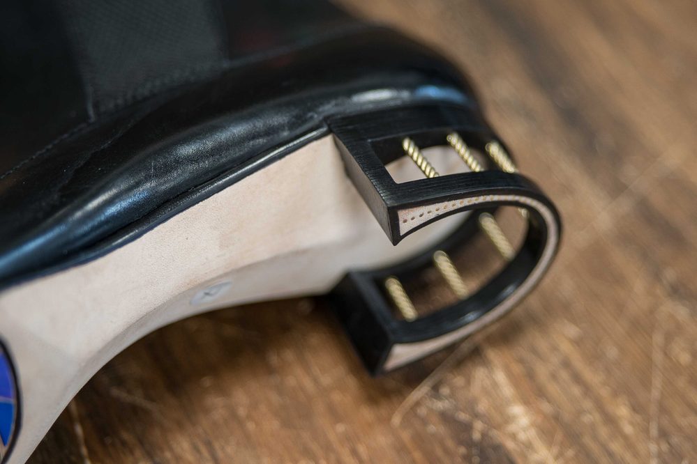 Close-up of a black leather shoe heel with gold detailing and a wooden base.