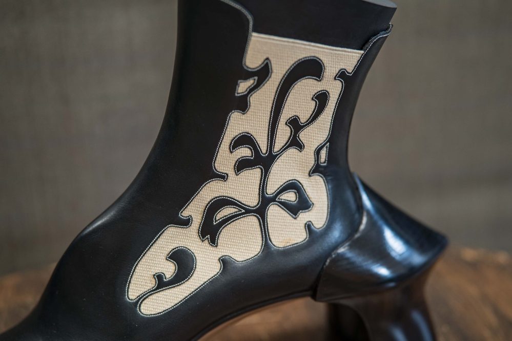 A black leather boot with a decorative beige pattern and contrasting stitching.