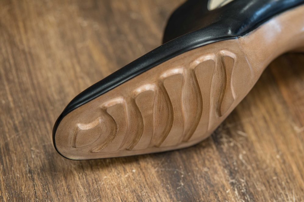 Close-up of a shoe's sole featuring a black edge and textured brown material with grooves.