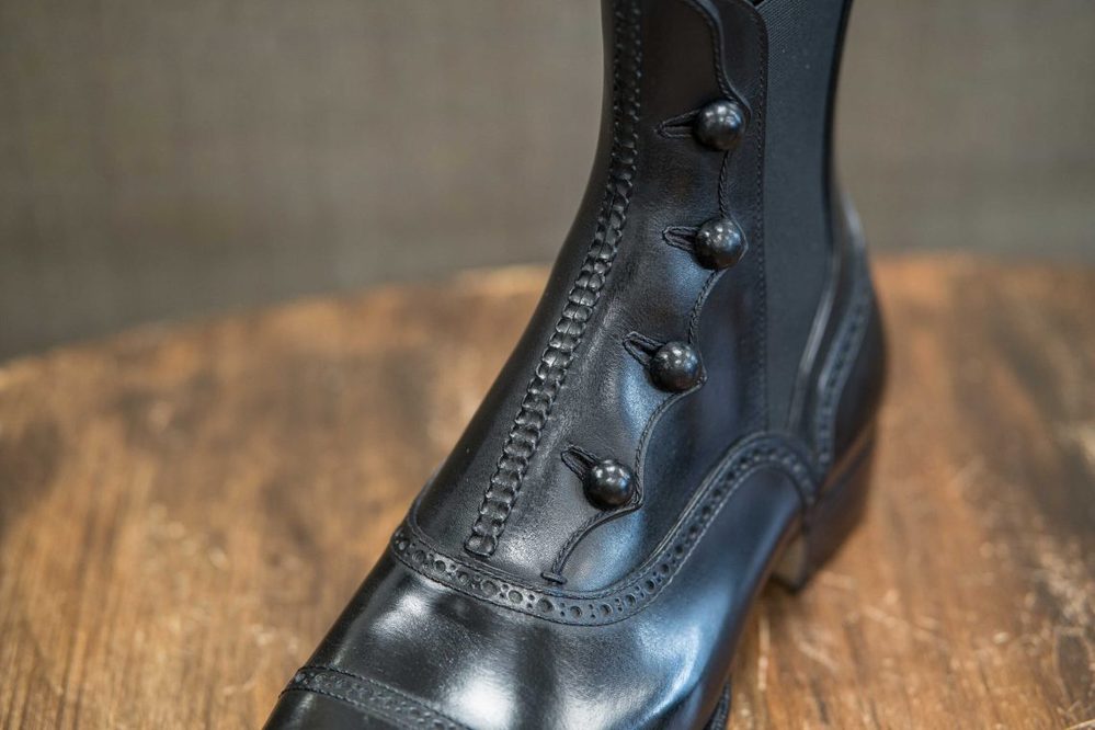 A close-up of a black leather boot featuring decorative buttons and intricate stitching.