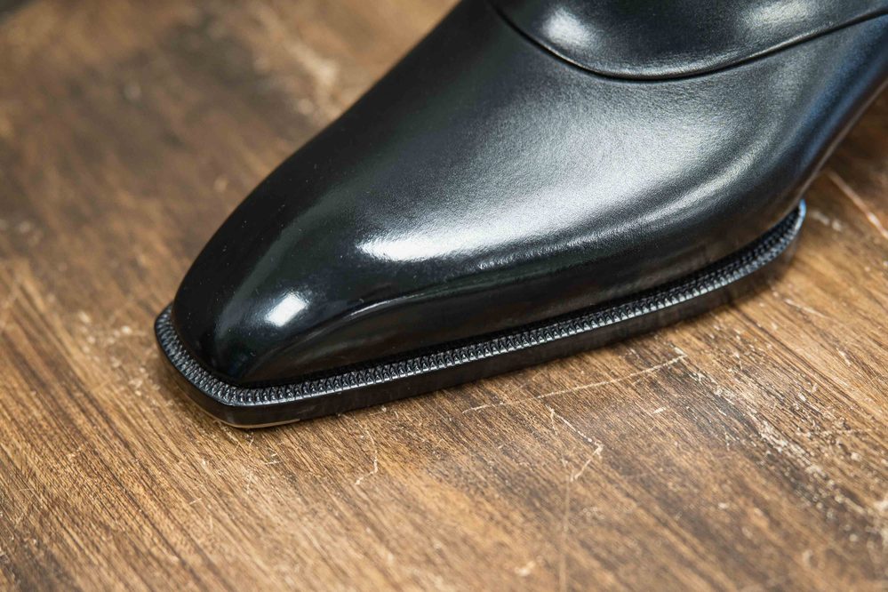 A close-up of a polished black leather shoe with a sleek pointed toe and a textured black sole.