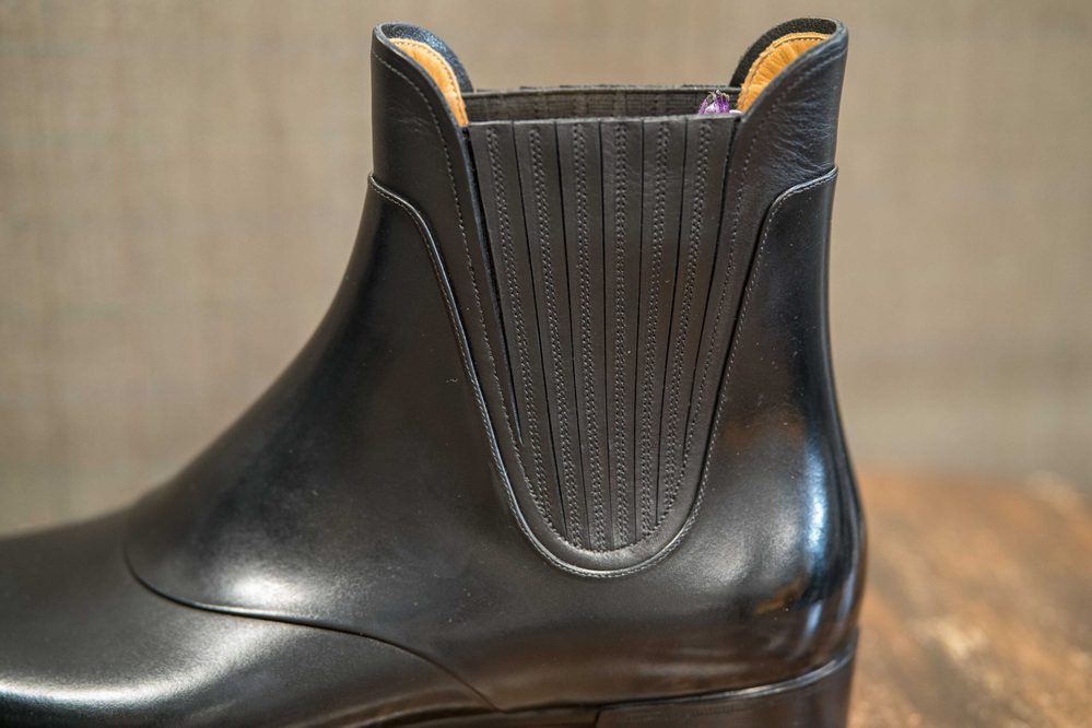 A close-up of a sleek black leather ankle boot featuring a ribbed elastic panel.