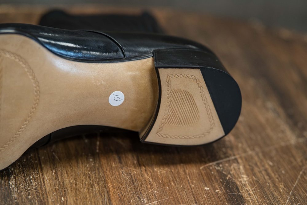 A close-up of a black shoe's heel showing a light brown sole with a round white label marked "10."