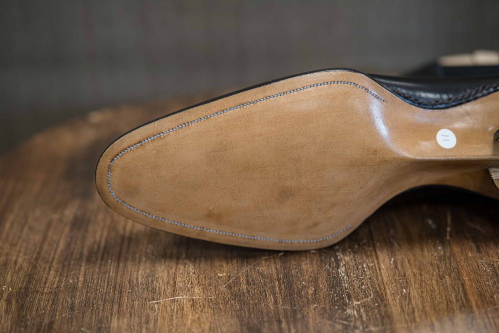 Close-up of a shoe sole made of light-colored leather, featuring blue stitching along the edge.