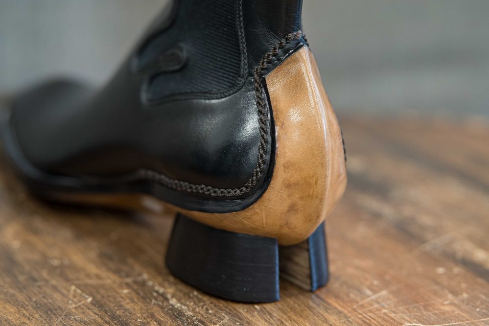 A close-up of a black leather shoe with a tan heel and intricate stitching.