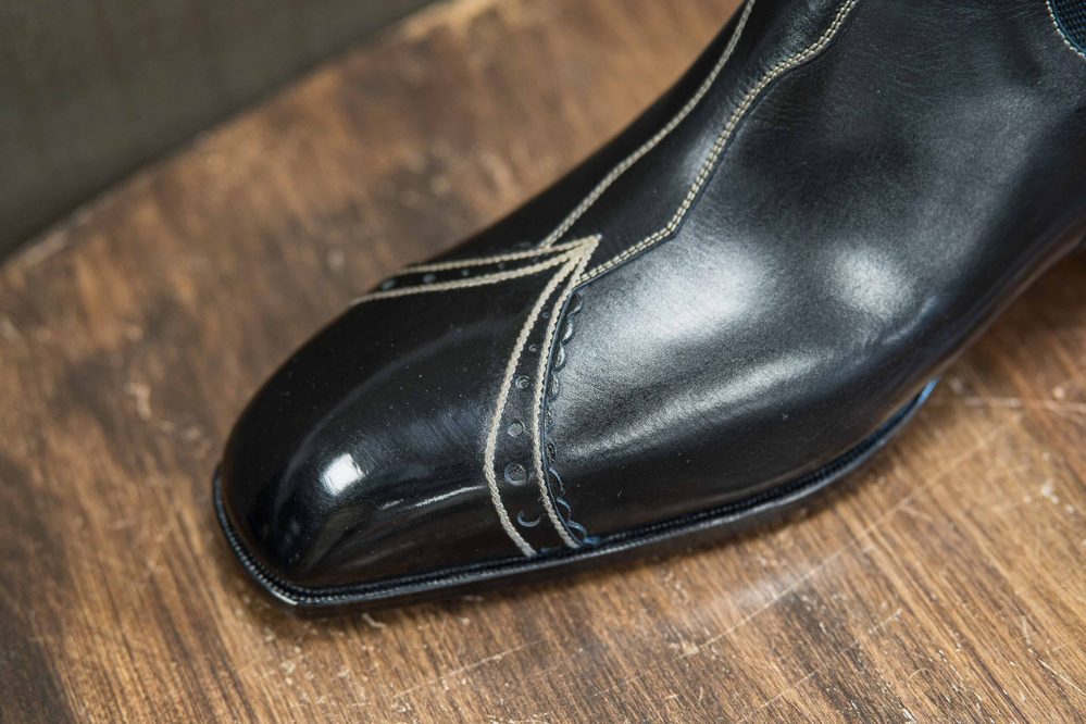 A polished black leather shoe with intricate stitching details.