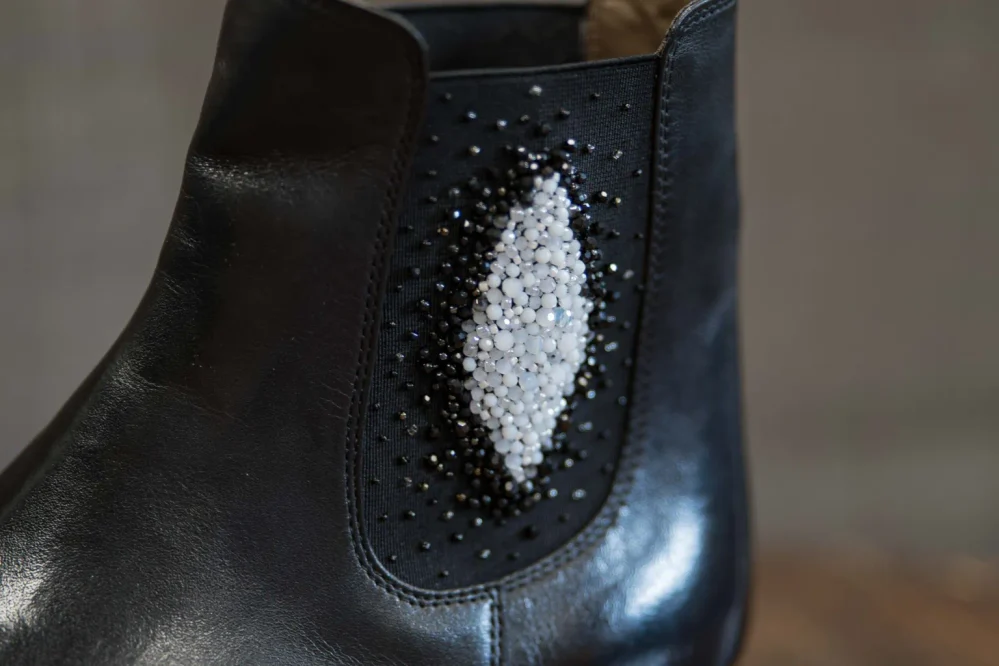 A black leather ankle boot featuring a decorative design of white and black beads.