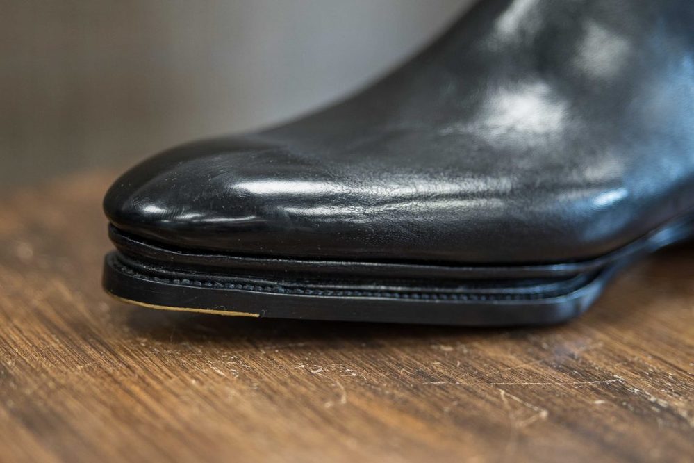 Close-up of a polished black leather shoe with a pointed toe and thin sole.