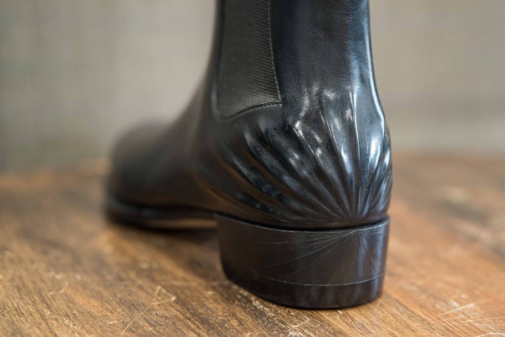 A close-up of a black leather boot with a decorative, ridged heel.