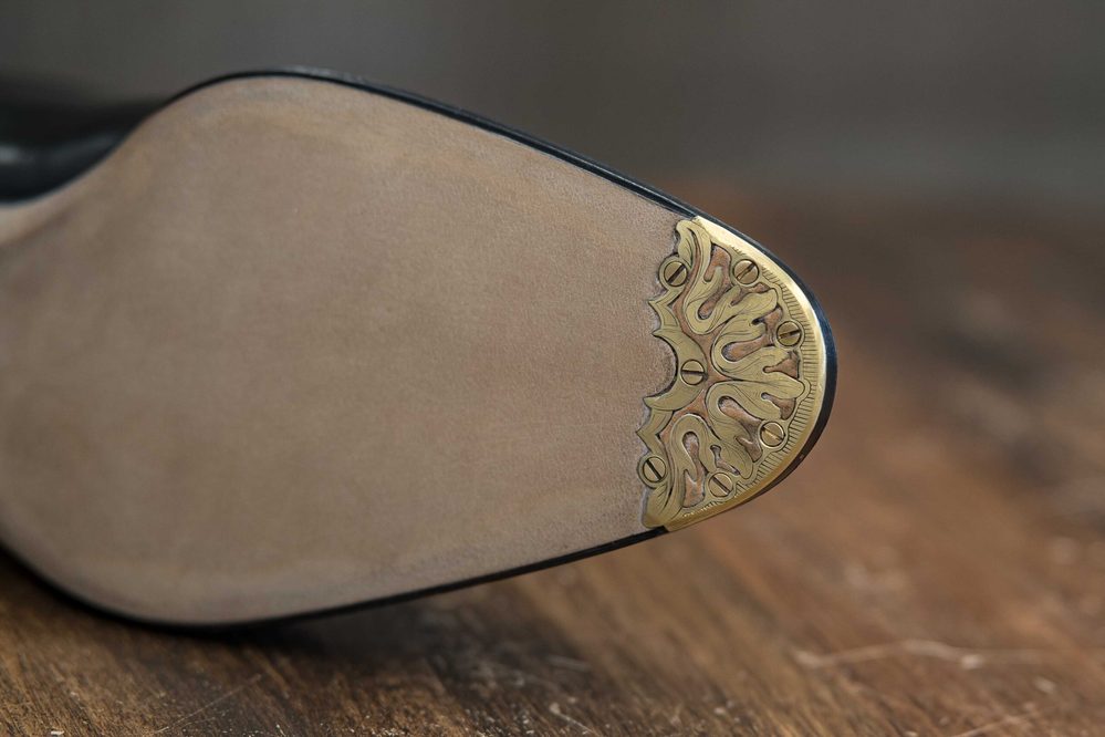 Close-up of a shoe sole featuring a decorative gold metal tip and a smooth beige surface.