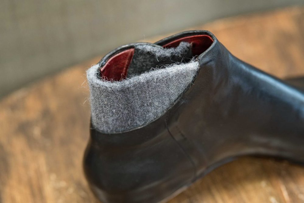 A close-up of a black leather shoe with a gray felt collar and red lining.