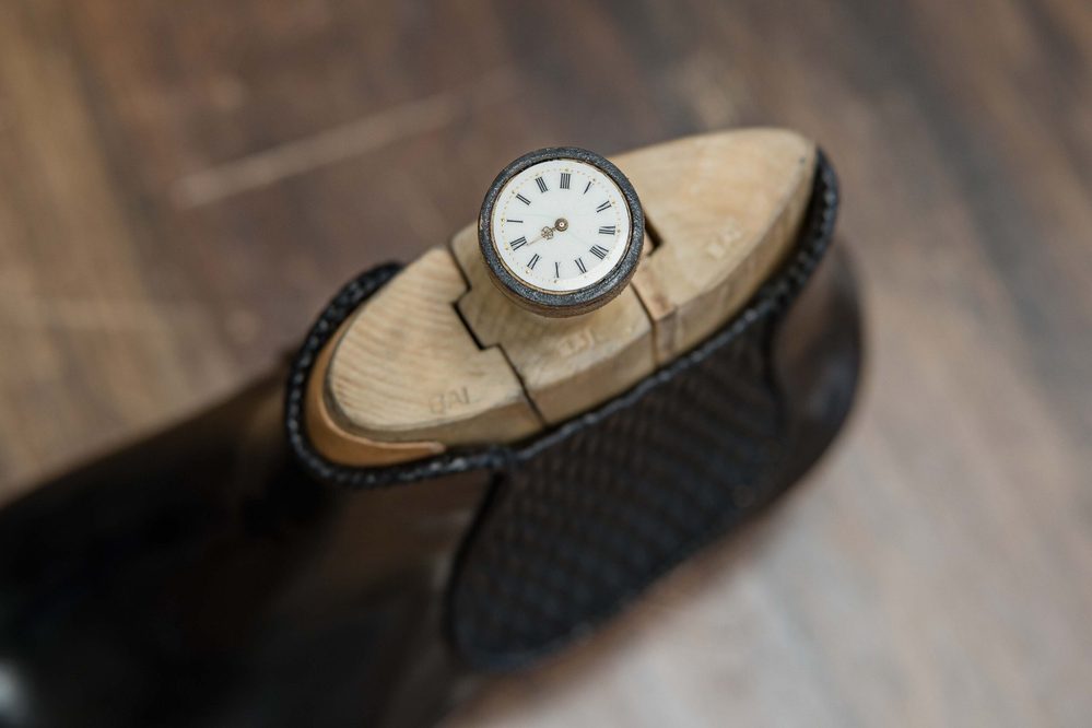 A close-up of a wooden shoe last with a small clock embedded at the top.
