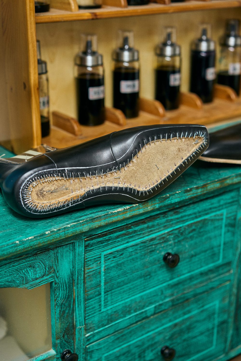 A black shoe with visible stitching and a cork sole rests on a teal wooden surface.