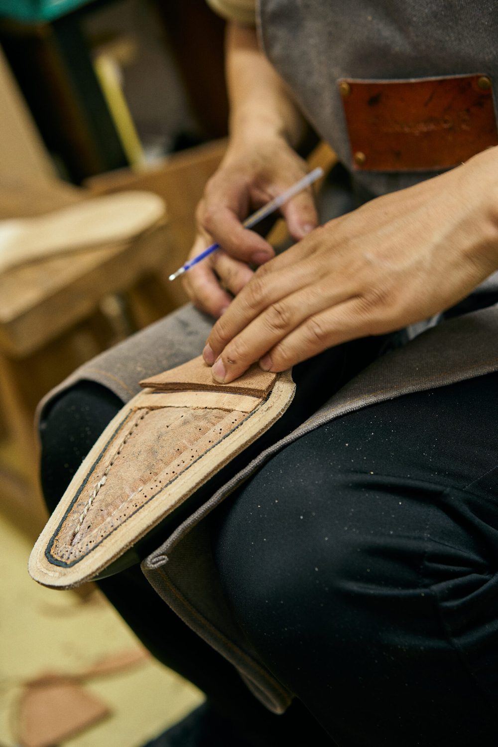 A person in an apron uses a pencil to position a piece of leather on a shoe sole.