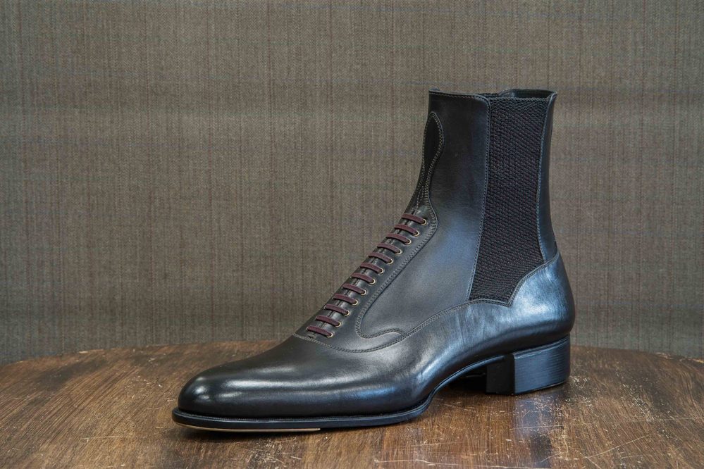 A sleek black leather ankle boot with maroon laces and a textured mesh panel.