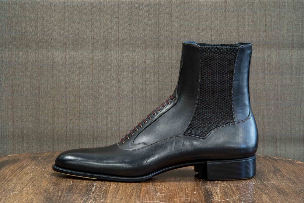 A sleek black leather boot with a textured side and burgundy laces.