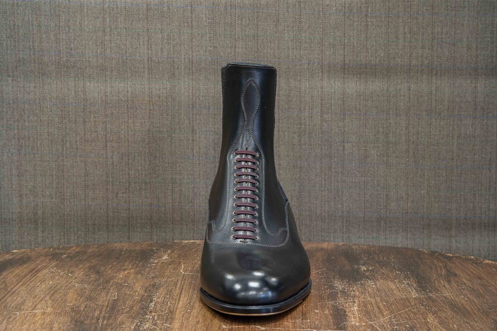 A polished black leather boot with burgundy laces.