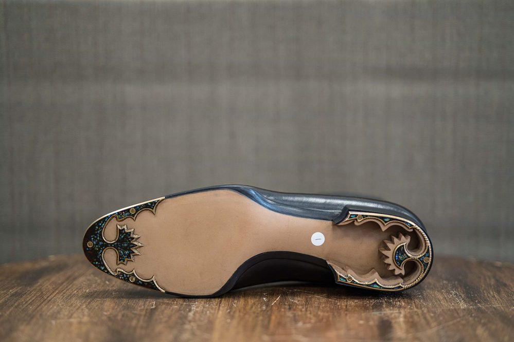 A black shoe sole with intricate gold and blue detailing on the heel.