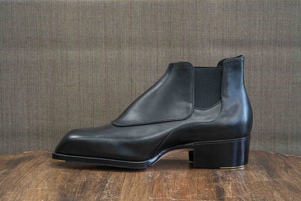 A sleek black leather boot with a low heel and elastic side panels.