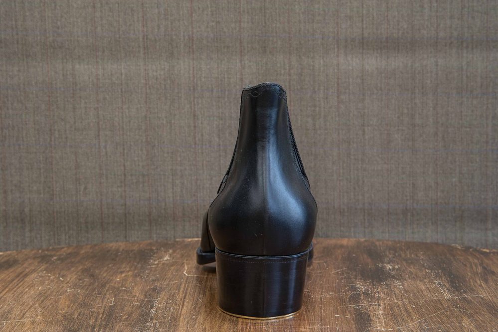 A polished black leather shoe with a high heel, viewed from the back.