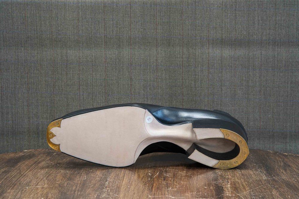 The image shows the sole of a black shoe with a gold metal plate and a smooth beige surface.