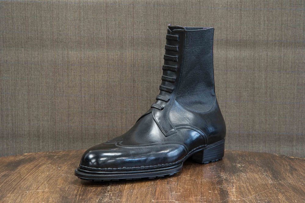 A polished black leather ankle boot with decorative lacing on the front.
