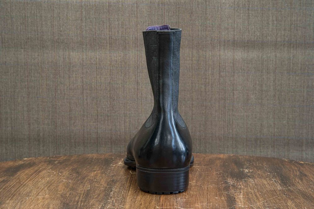 A pair of black leather boots viewed from the back, featuring a smooth finish and a sturdy heel.