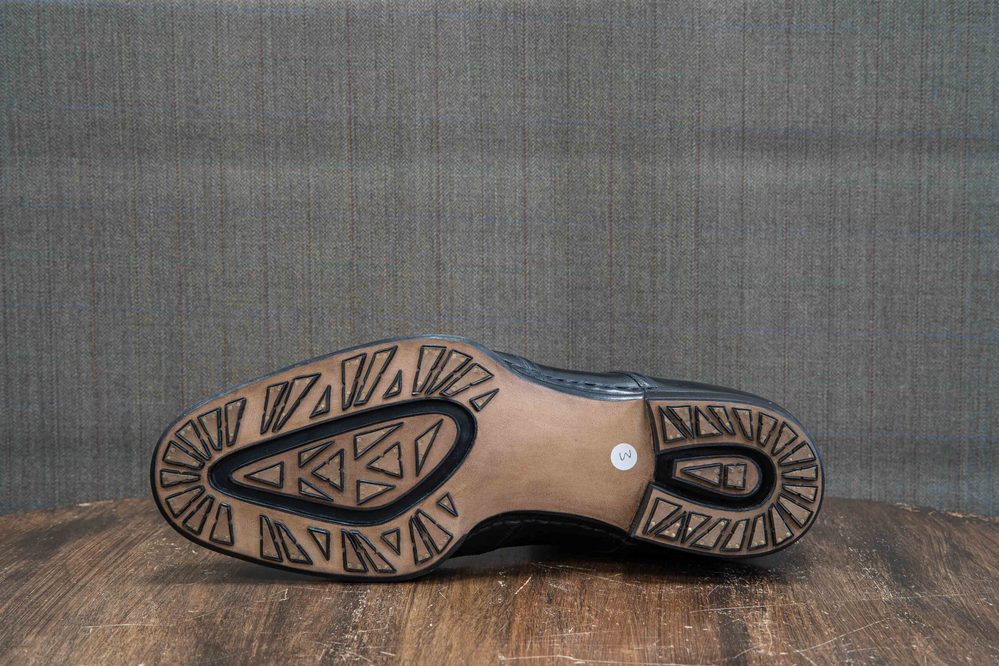 The image shows the sole of a black shoe with a textured brown rubber outsole and a label marked "M."