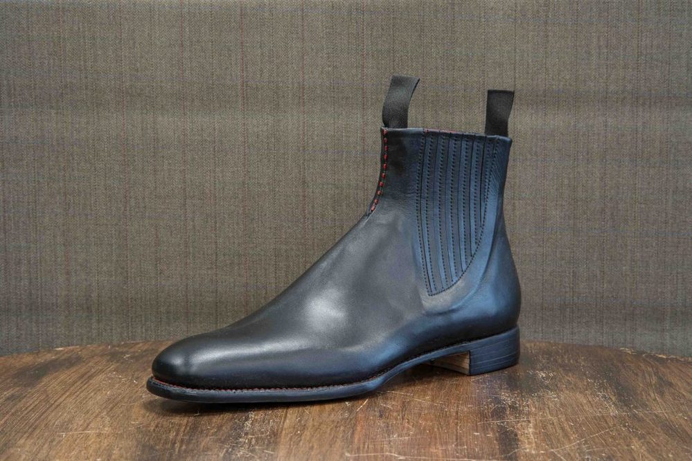 A sleek black leather Chelsea boot with elastic side panels and red stitching.