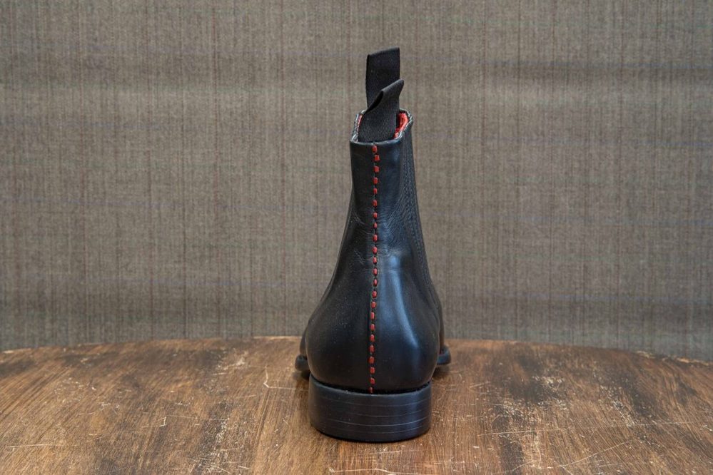 A black leather boot with red stitching, shown from the back.