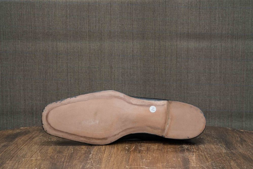 The image shows the bottom of a black dress shoe with a light brown leather sole.