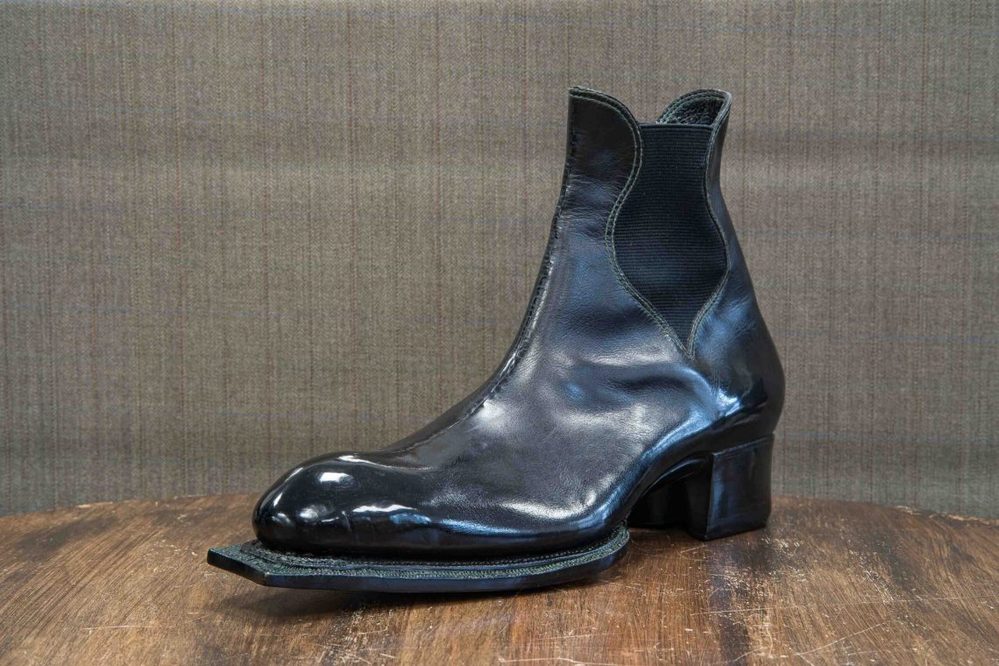 A shiny black leather boot with a low heel and elastic side panels.