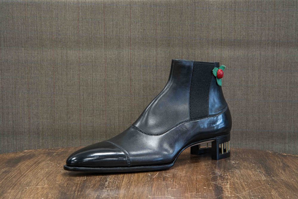 A black leather ankle boot with a mesh panel and a decorative rose on the heel.