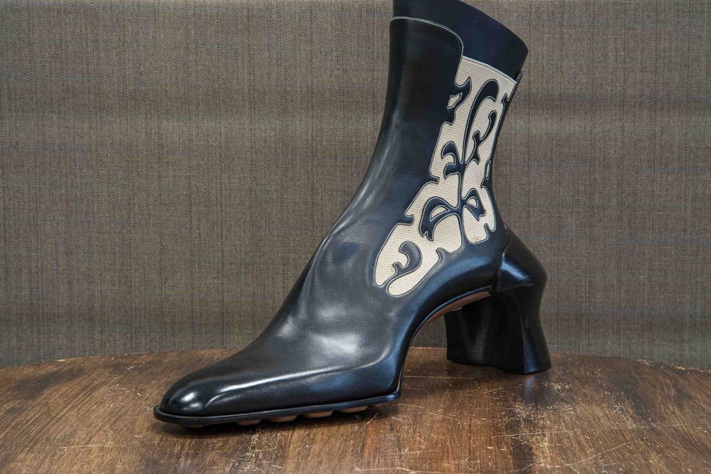 A black leather ankle boot with a decorative cream pattern and a chunky heel.