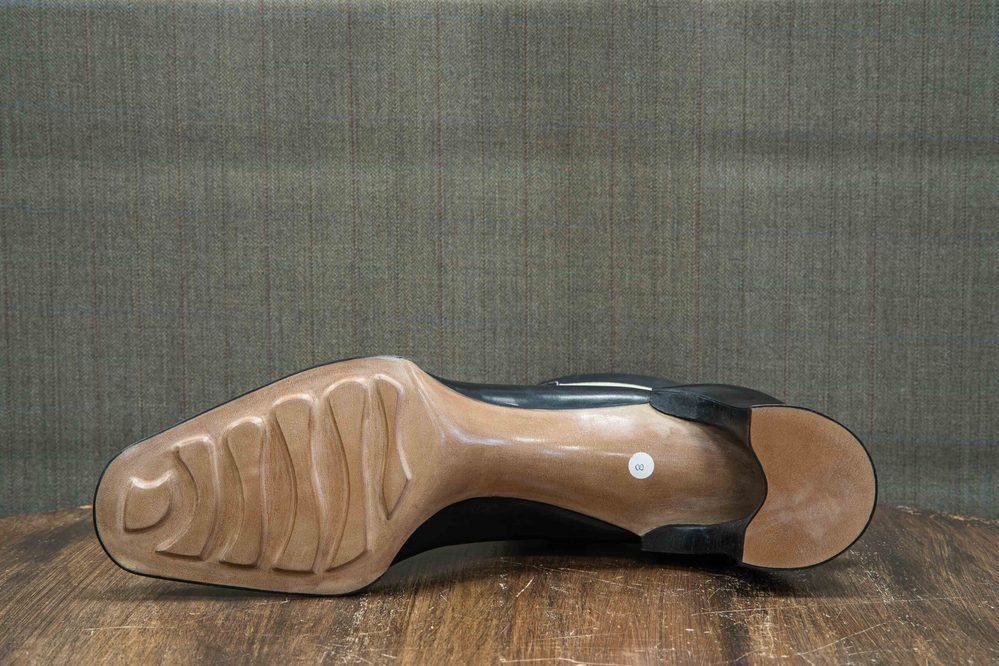 The image shows the sole of a black shoe with a smooth brown heel and a textured rubber grip pattern.