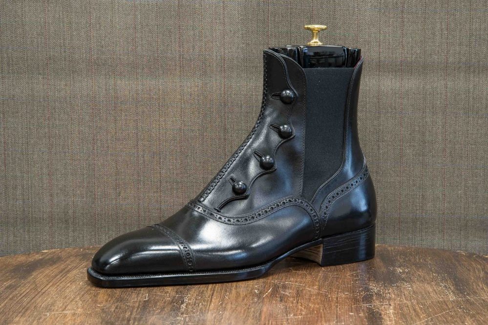 A polished black leather ankle boot featuring decorative buttons and elastic side panels.