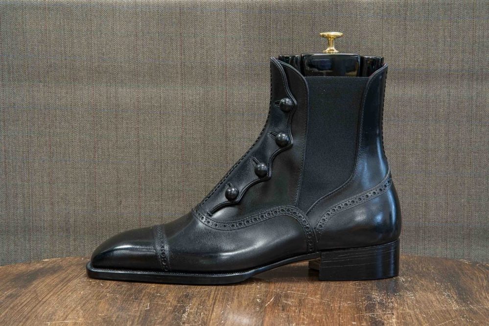 A black leather ankle boot with decorative buttons and a polished toe.