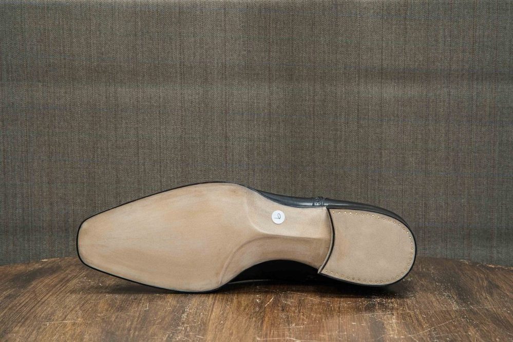 The image shows the sole of a black shoe with a smooth beige outsole and a white label.