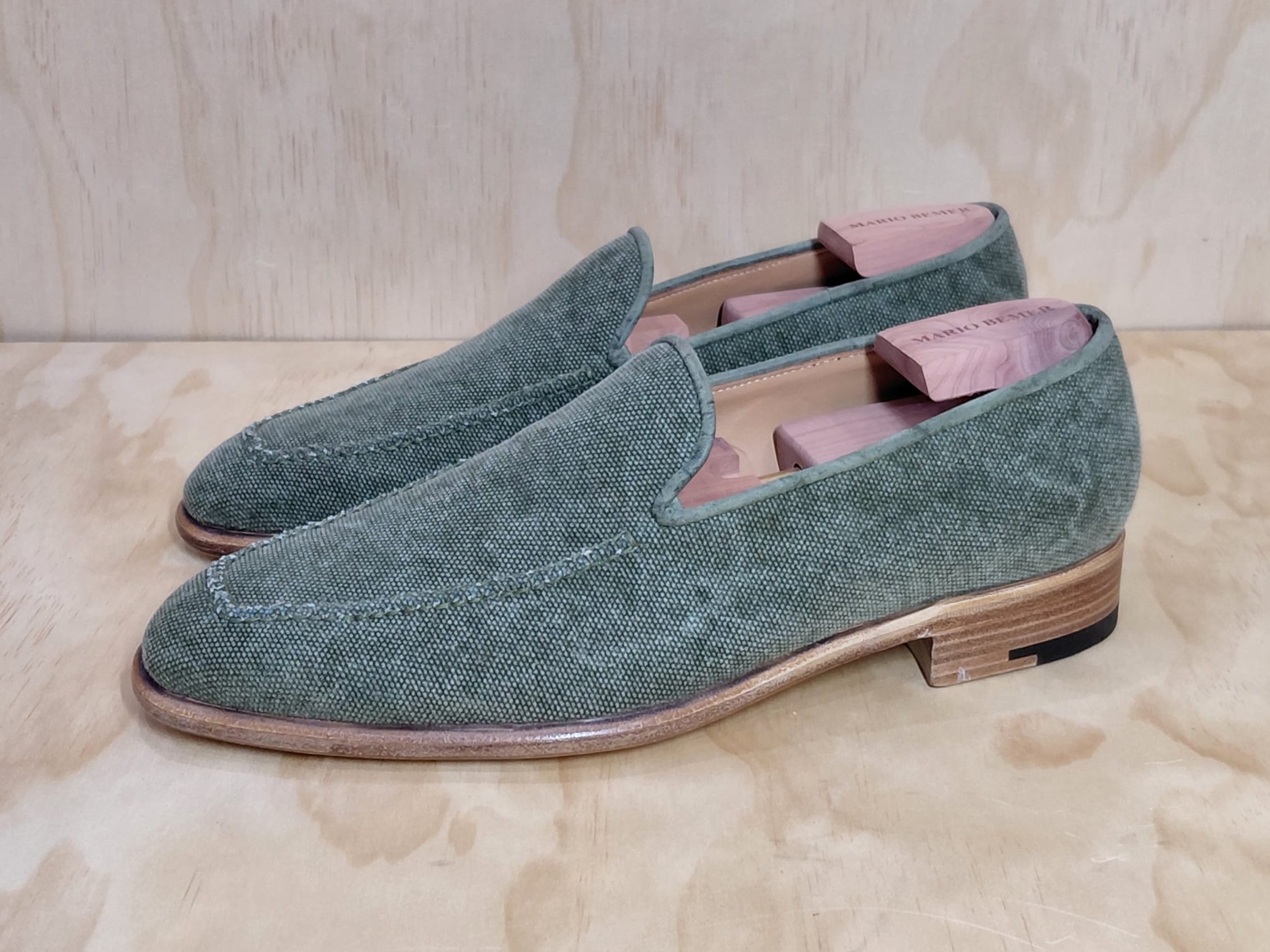 Green canvas loafers with a wooden shoe tree inside.
