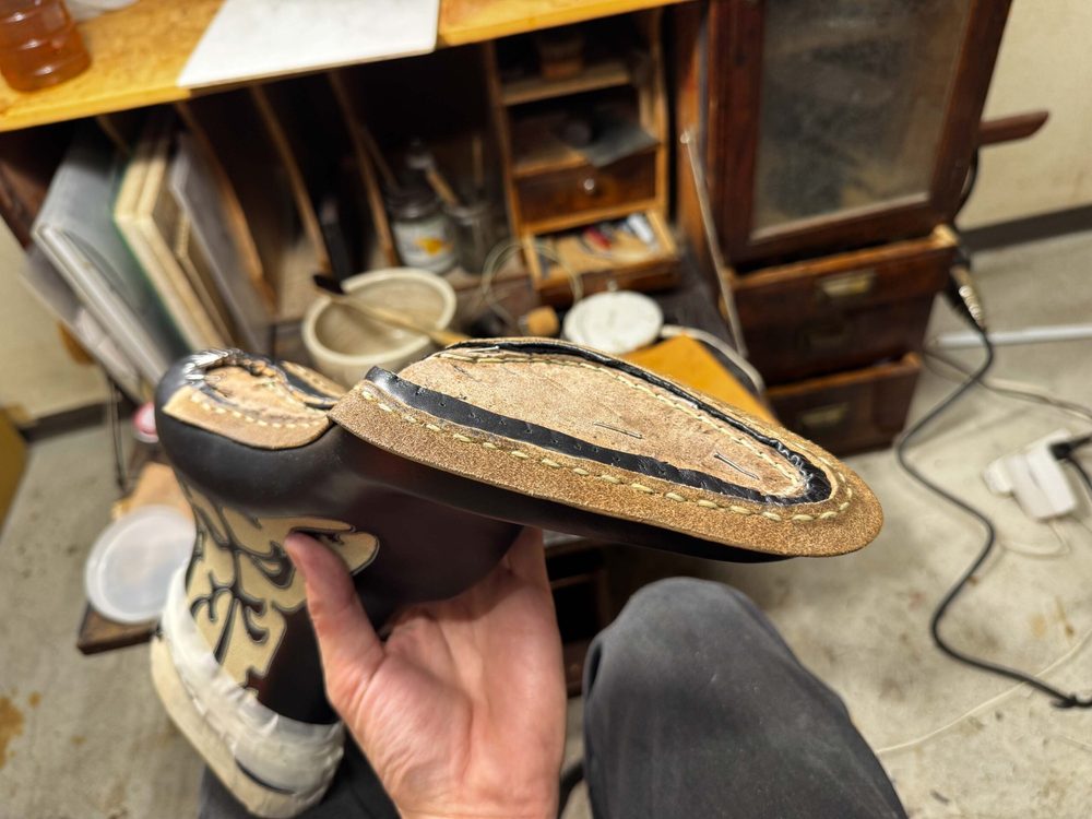 A close-up of a handcrafted shoe sole featuring dark leather and visible stitching details.